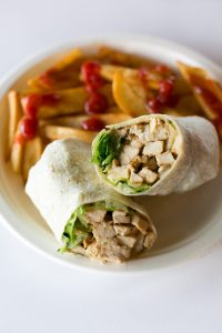 A white plate with french fries and a chicken wrap.