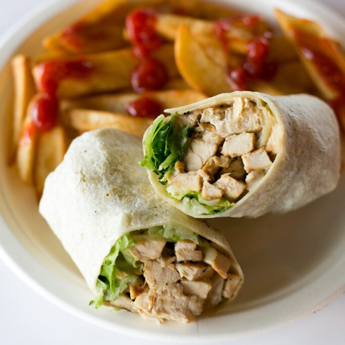 A white plate with french fries and a chicken wrap.